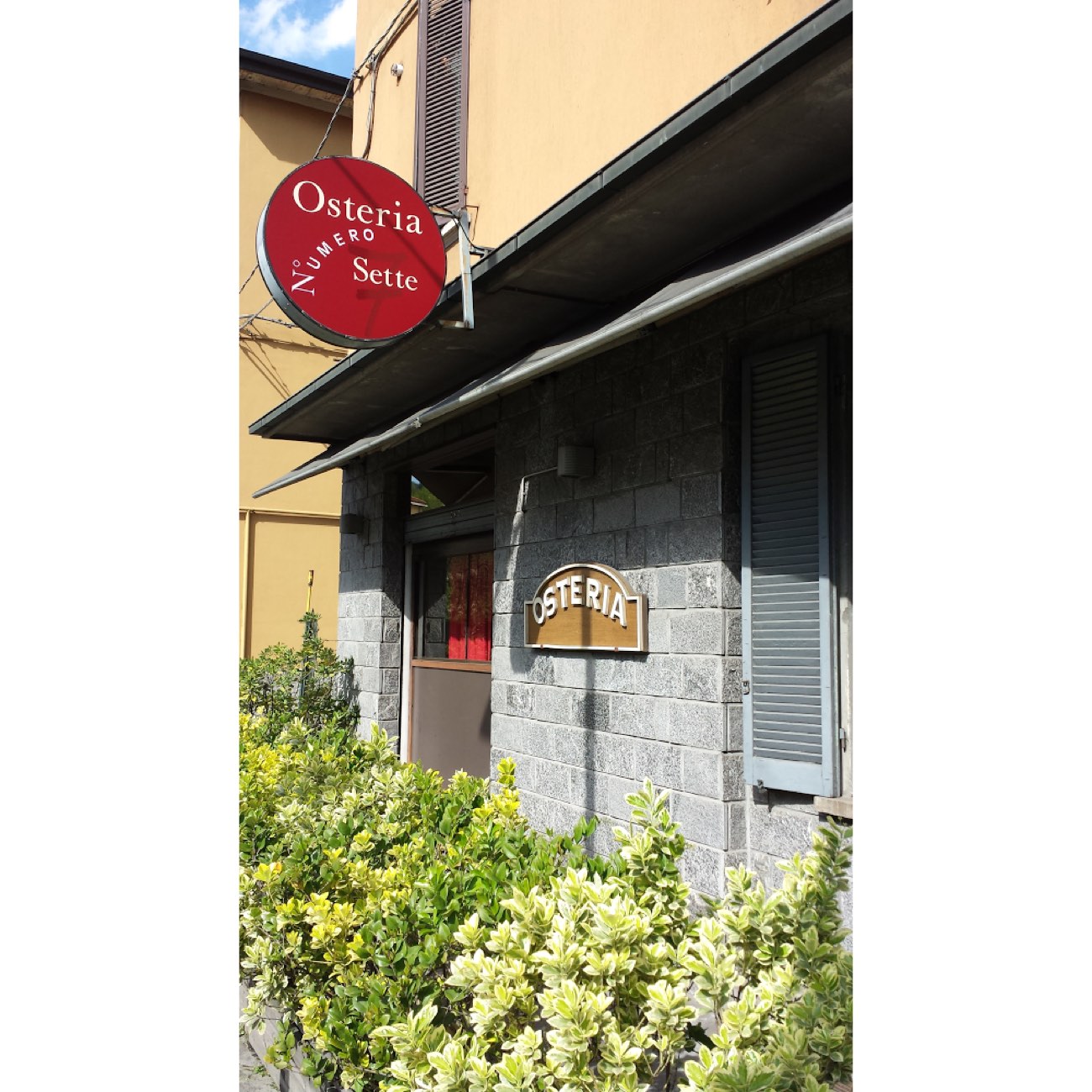 La facciata in pietra dell'Osteria Numero Sette con l'insegna smaltata bordeaux